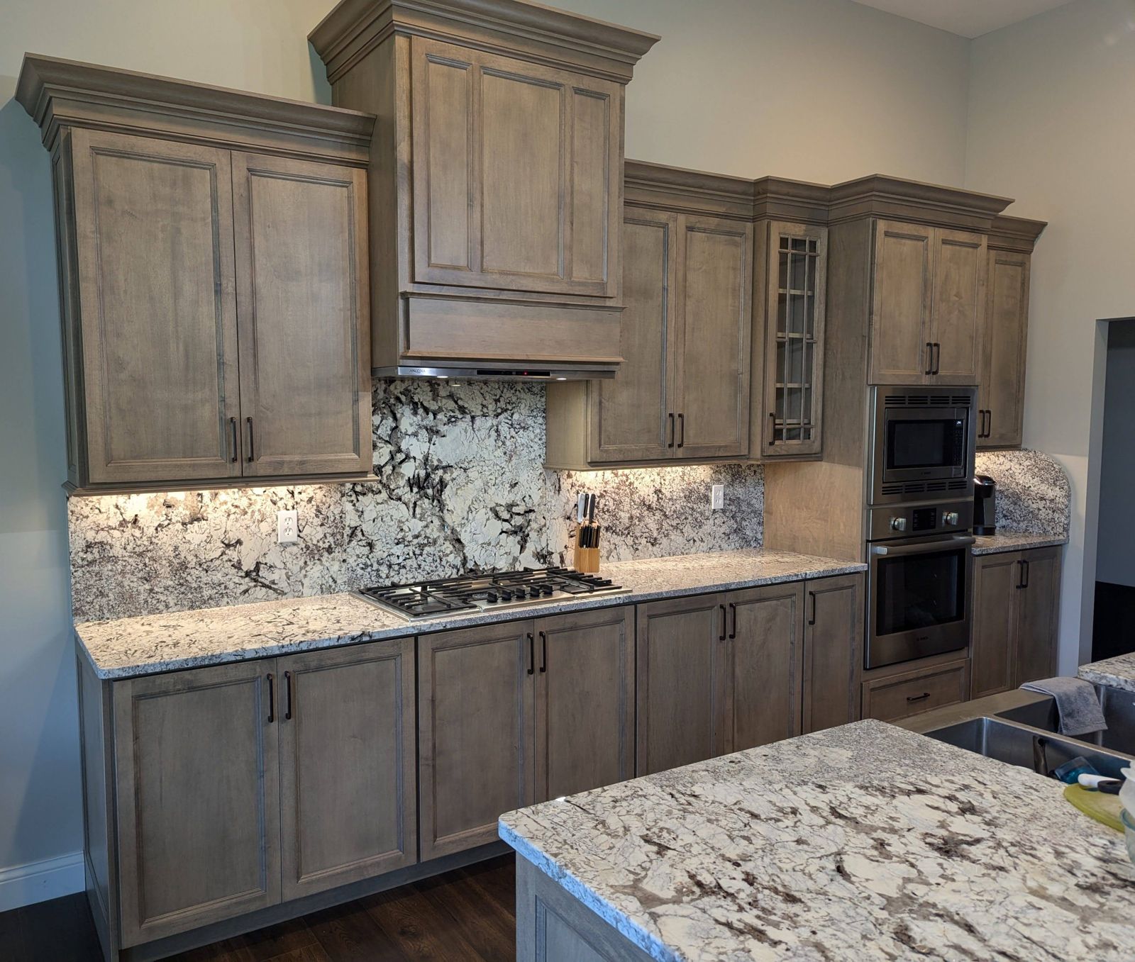 Gray stained cabinetry with a range hood and granite backsplash
